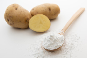 Fototapeta na wymiar Close-up of potato starch or flour powder in wooden spoon on white background