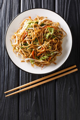 Traditional recipe for fried chow mein noodles with vegetables close-up on a plate. Vertical  top view