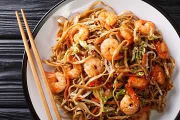 Stir fried chow mein noodles with shrimp, vegetables and sesame seeds close-up on the table. Horizontal top view