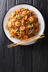 Tasty chow mein noodles with shrimp, vegetables and sesame seeds close-up on a plate. Vertical top view