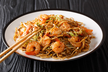 Authentic chow mein noodle fried with shrimp, vegetables and sesame seeds close-up on a plate on the table. horizontal