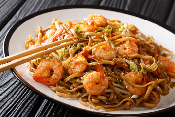 Stir fried chow mein noodles with shrimp, vegetables and sesame seeds close-up on the table. horizontal
