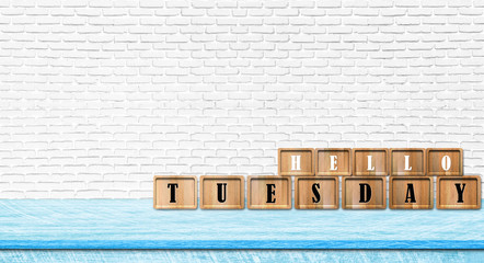 Hello Tuesday alphabet letters put on blue table with white brick wall background. Copy space for text.