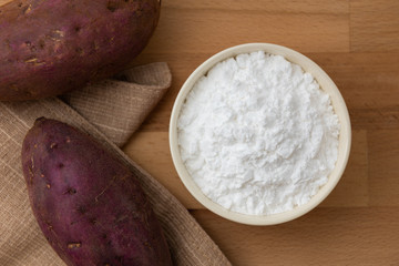 Top view of sweet potato starch in white bowl with sweet potato wooden table background
