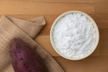 Top view of sweet potato starch in white bowl with sweet potato wooden table background