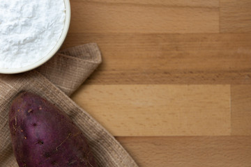 Top view of sweet potato starch in white bowl with sweet potato wooden table background
