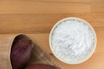 Top view of sweet potato starch in white bowl with sweet potato wooden table background