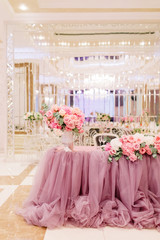 Table decoration with fresh flowers in pastel colors. Elegant dining table in peach-pink color. Luxurious flowers composition. Indoors wedding. Tablecloth lilac color. Beautiful table setting.