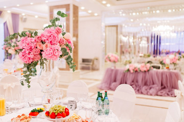 Table decoration with fresh flowers in pastel colors. Elegant dining table in peach-pink color. Luxurious flowers composition. Indoors wedding. Tablecloth lilac color. Beautiful table setting.