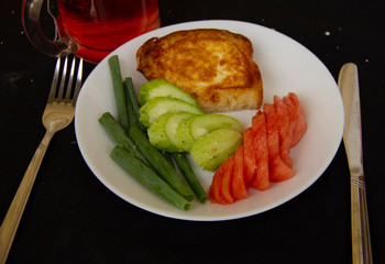toast fried in a beaten egg lies on a white plate with chopped tomatoes, cucumbers and green onions. Great breakfast. serving dishes on a black tablecloth