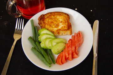 toast fried in a beaten egg lies on a white plate with chopped tomatoes, cucumbers and green onions. Great breakfast. serving dishes on a black tablecloth