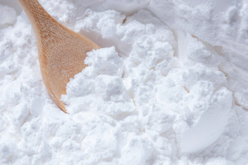 Close-up of tapioca starch or flour powder in wooden spoon on white background