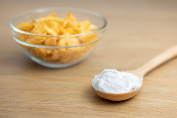 Close-up of starch or flour powder in wooden spoon with cornflakes on wooden background