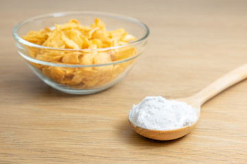 Close-up of starch or flour powder in wooden spoon with cornflakes on wooden background