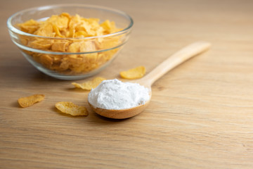 Close-up of starch or flour powder in wooden spoon with cornflakes on wooden background