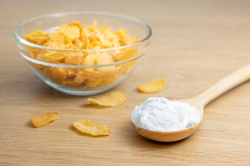 Close-up of starch or flour powder in wooden spoon with cornflakes on wooden background