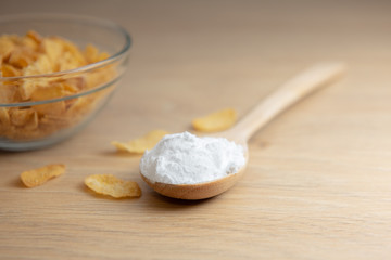 Close-up of starch or flour powder in wooden spoon with cornflakes on wooden background