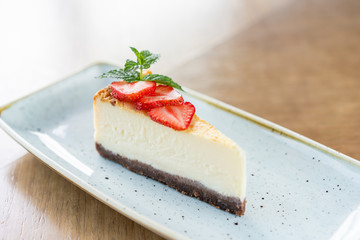 Piece of delicious cheesecake with strawberry and mint leaves on white plate.