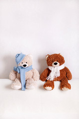 Children's toys teddy bears sitting on a white sofa in a knitted white and blue scarf and hat.