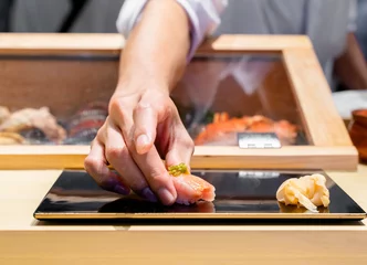 Selbstklebende Fototapeten Japanese Sushi Chef serve sushi by hand on the black shimmer plate. (Omakase sushi course) Selective focus on sushi. © Sugrit