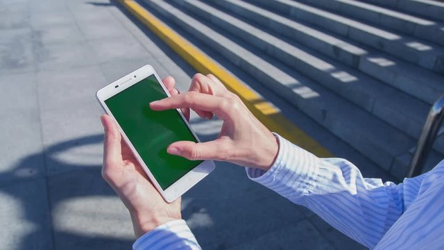 Hight quality 10bit footage of Young woman uses SmartPhone with green screen staying in city square. Made from 14bit RAW