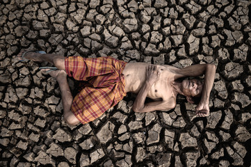 Elderly men lay flat on their hands, on the stomach and forehead, on dry soil, global warming.