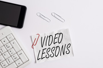 Text sign showing Video Lessons. Business photo showcasing Online Education material for a topic Viewing and learning White pc keyboard with empty note paper above white background and mobile phone