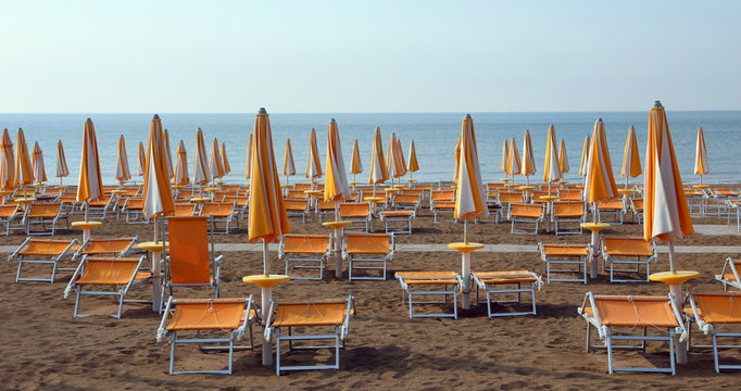closed umbrellas with deckchairs on the beach without people in