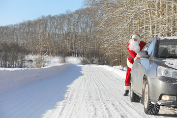 Santa Claus comes with gifts from the outside. Santa in a red suit with a beard and wearing glasses is walking along the road to Christmas. Father Christmas brings gifts to children.