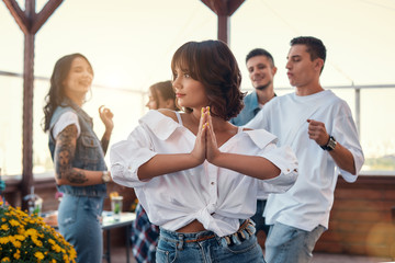 Fototapeta na wymiar Feeling happy and peaceful. Pretty and young woman in white shirt is holding palms together while enjoying party on rooftop terrace with friends