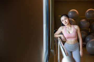 A woman standing relaxed, hands placed on a steel rail in the gym.