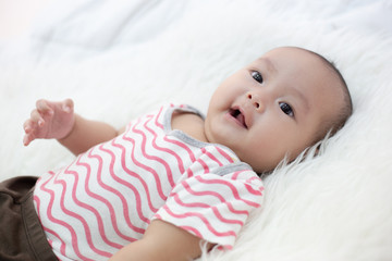 The baby wears a red shirt on the bed.