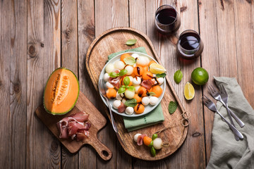Melon, mozzarella, prosciutto salad, appetizer or snack, two glasses of red wine, party food, top...