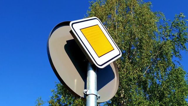 A yellow square sign showing priority road seen from bellow, stuck on the back of another circular sign