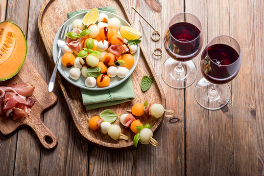 Two glasses of red wine, melon, mozzarella, prosciutto appetizer or snack, summer salad with cantaloupe melon