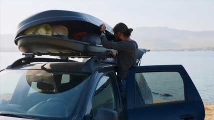 Young bearded man taking out a camping equipment from car roof box