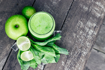 Green apple smoothie in glass and kale leaves on wooden table