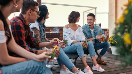 Barbecue. Young cheerful people chatting and drinking cocktails while sitting on the roof