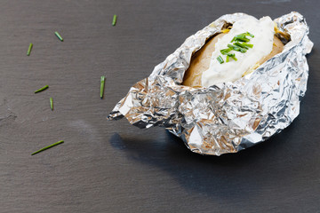 Ofenkartoffel in Aluminiumfolie mit Kräuterquark auf einer Schiefertafel serviert