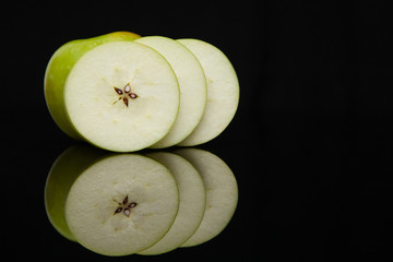 green apple slices on a black background with reflection