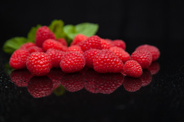 raspberries with mint leaves reflected on a black mirror table