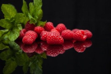 raspberries with mint leaves reflected on a black mirror table
