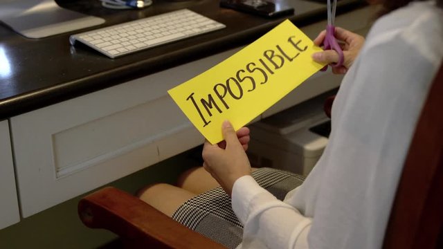 Hands using scissors to remove the word Impossible to Possible concept for self belief, positive attitude and motivation