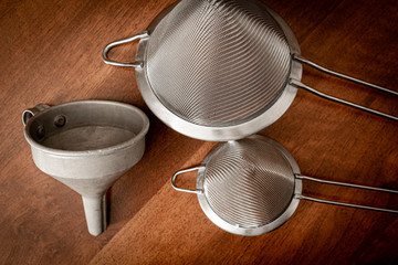 two metal strainers and a metal funnel