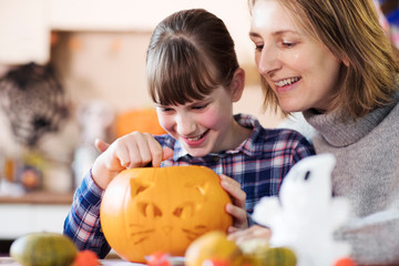 Fototapeta premium Mother And Daughter Carving Halloween Lantern From Pumpkin At Home