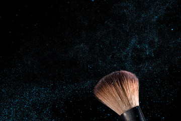 cosmetic brush and sprayed cloud of cosmetics on a black background