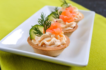 Tartlets with cream cheese and salted salmon on a white plate. Tasty light snack for a party. Finger Food.