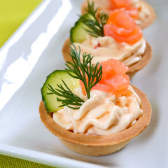 Tartlets with cream cheese and salted salmon on a white plate. Tasty light snack for a party. Finger Food.
