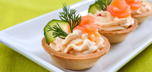 Tartlets with cream cheese and salted salmon on a white plate. Tasty light snack for a party. Finger Food.