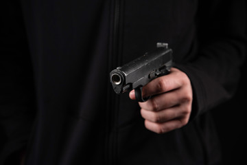 Gun in hand on black background. The threat of a firearm during a robbery on a dark street. Assault with a semiautomatic weapon.